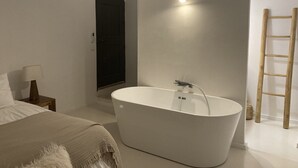 A modern bathroom with a freestanding bathtub, a wooden ladder, and a small bedside table with a lamp.
