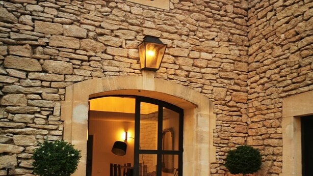 A stone building with a large arched entrance, two potted trees, and a lantern above the door.