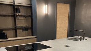 A modern kitchen with a central island, bar stools, a built-in stove, and a wooden door.