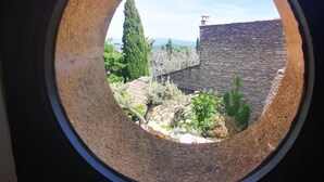 A round window with a view of a stone building and greenery.