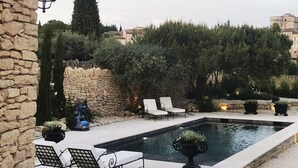 A pool area with lounge chairs, a stone wall, and a view of the surrounding landscape.