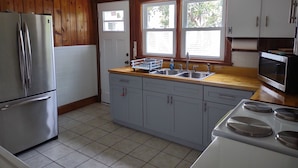 Una cocina con paneles de madera, un refrigerador de acero inoxidable, un lavamanos y una estufa.