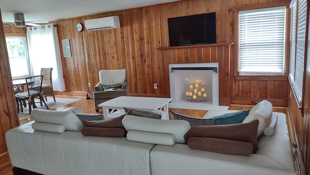 Una sala de estar acogedora con un sofá blanco, una chimenea, paneles de madera y un televisor.