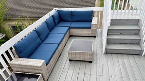 A covered deck with a sectional sofa and a small table.