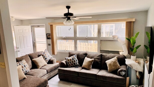 A living room with a brown sectional sofa, a ceiling fan, and large windows.