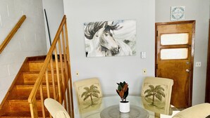 A dining area with a glass table, two chairs with palm tree designs, a wooden staircase, and a door with a frosted glass panel.