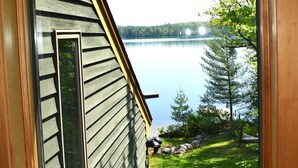 Une vue depuis une fenêtre d’une maison dotée d’une terrasse surplombant un lac et des arbres.
