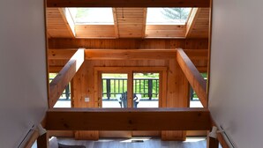 Une pièce aux hauts plafonds, dotée d’une lucarne, de poutres en bois et offrant une vue sur la terrasse extérieure.