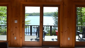 Une cabane en bois dotée d’une grande porte vitrée donnant sur une terrasse qui offre une vue sur un lac.
