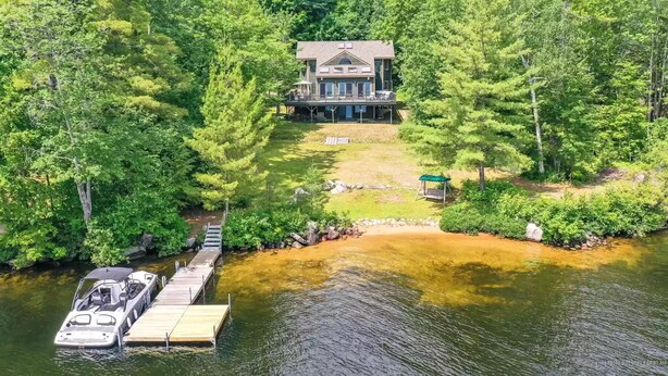 Un chalet au bord du lac, doté d’un quai, et entouré d’une forêt dense.