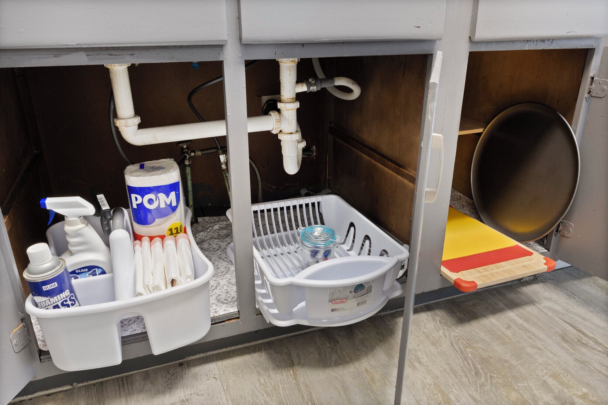 A kitchen sink area with cleaning supplies, a dish rack, and a cutting board.
