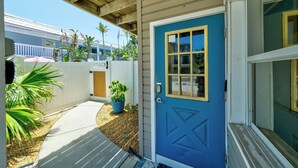 Une porte bleue avec un cadre jaune, une clôture blanche faite de piquets et un pot de fleurs au premier plan.