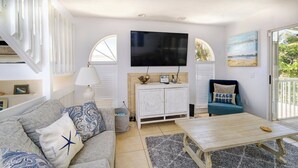 Un salon avec un canapé, une table basse, un téléviseur et un fauteuil sur le thème de la plage.