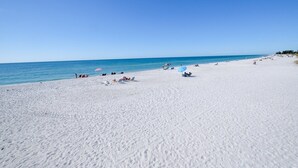 Une vaste plage de sable fin, avec une eau d’un bleu limpide, des parasols et des gens qui se détendent.
