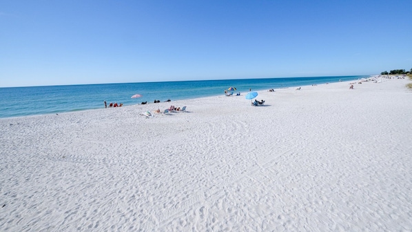 Uma extensa praia de areia com águas azul-claras, guarda-sóis e pessoas relaxando.