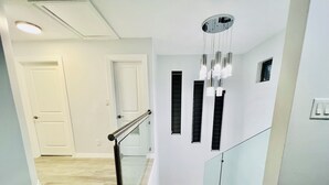 Un escalier moderne avec des rampes en verre et une main courante en métal, menant à un palier agrémenté d’un luminaire décoratif.