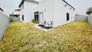 Une maison moderne à deux étages, dotée d’un toit plat, d’un patio couvert et d’une cour arrière clôturée.