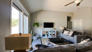 Ein Wohnzimmer mit Deckenventilator, Flachbildfernseher, Bücherregal und einer Couch.