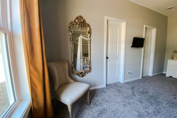A bedroom with a large ornate mirror, a chair, a dresser, and a television on the wall. - Modern, Family-Friendly Space, Quick KC Downtown, Driveway, Quiet Road & Nature! (Kansas City)