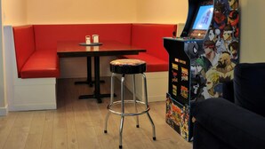 Een kamer met een rode gestoffeerde bank, een kleine tafel met een fles, een kruk en een speelautomaat met personages van Marvel en Capcom.