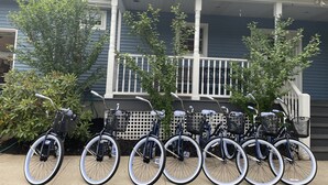 Une rangée de vélos équipés de paniers est garée devant une maison dotée d’un porche.