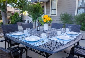 Une table de jardin ronde, préparée pour un repas, avec de l’assiette blanche, des couverts et des sets de table bleus.