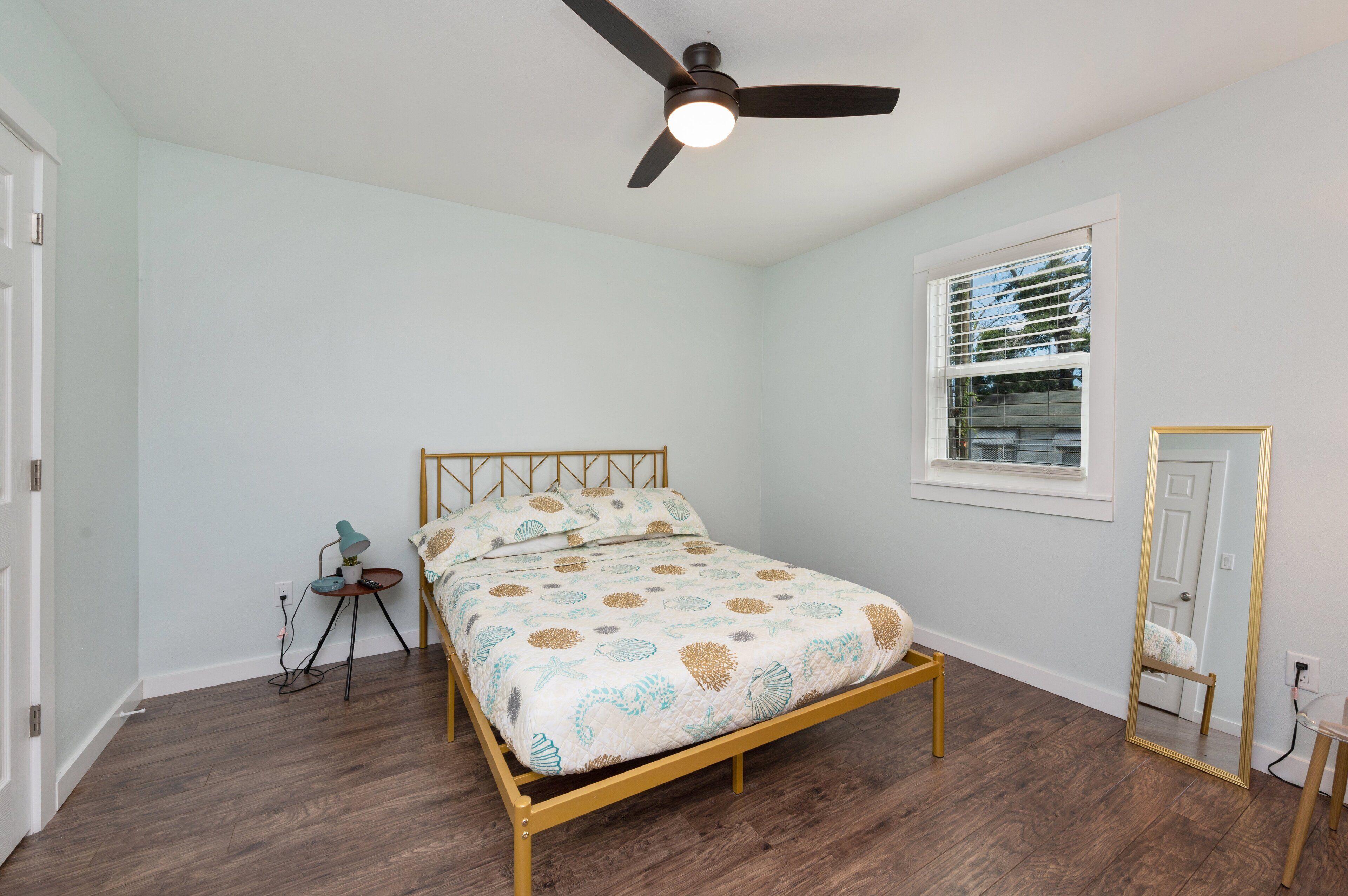 A bedroom with a bed, a ceiling fan, a window with blinds, and a mirror.