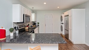 A modern kitchen with white cabinets, a granite countertop, stainless steel appliances, and a door leading to another room. - Stylish 2 bedroom home close 2 Dtown, NAS, and BCH (Pensacola)