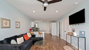 A modern living room with a black leather sofa, a glass coffee table, and a ceiling fan. - Stylish 2 bedroom home close 2 Dtown, NAS, and BCH (Pensacola)
