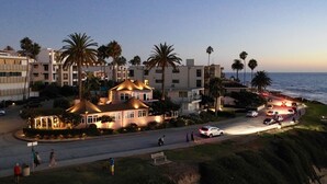 A beachfront hotel with multiple buildings, palm trees, and a road with cars and pedestrians.