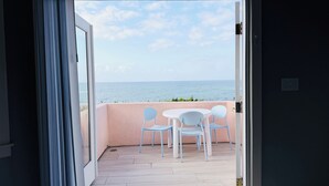 An open door leading to a balcony with a view of the sea, a round table, and four chairs.