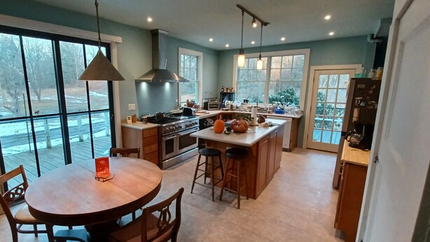 A modern kitchen with a large island, double ovens, and a dining area with a table and chairs. - Historic Stockbridge Villa on 25 acres (Stockbridge)