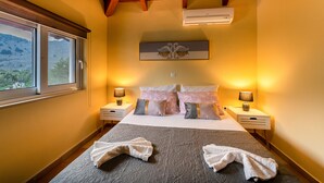 Una cama bien hecha con almohadas, una lámpara de noche y vistas al exterior a través de una ventana.