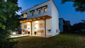 Una casa de dos pisos con un porche cubierto, mobiliario exterior y un césped cuidado.