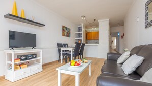 A modern living room with a flat-screen TV, a white coffee table, a leather sofa, and a dining area with a table and chairs. - SOL - Nice apartment close to the beach and leisure area. Free WiFi. (Alcúdia)