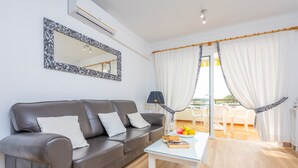 A modern living room with a grey leather sofa, a glass coffee table with books and fruit, a large mirror, and white curtains. - SOL - Nice apartment close to the beach and leisure area. Free WiFi. (Alcúdia)