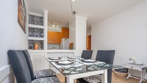 A dining area with a glass table set for four, surrounded by dark upholstered chairs. A kitchen with wooden cabinets and a white refrigerator is visible in the background. - SOL - Nice apartment close to the beach and leisure area. Free WiFi. (Alcúdia)