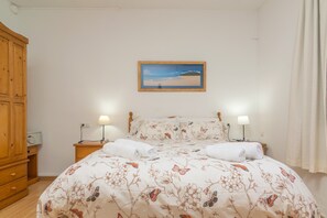 Une chambre à coucher avec une couvre-lit à motifs floraux, deux lampes de chevet, une armoire en bois et un tableau encadré au mur.