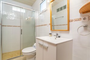 Ein Badezimmer mit Duschkabine, Toilette, Waschbecken mit Spiegel und Handtuchhalter.