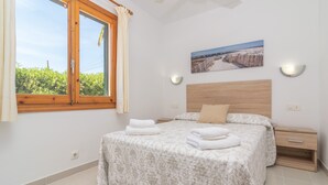 A bedroom with a large bed, a window with curtains, a nightstand, a wall-mounted light, and a painting. - VILLA VICTORIA - Charming house with shared pool. (Alaior)