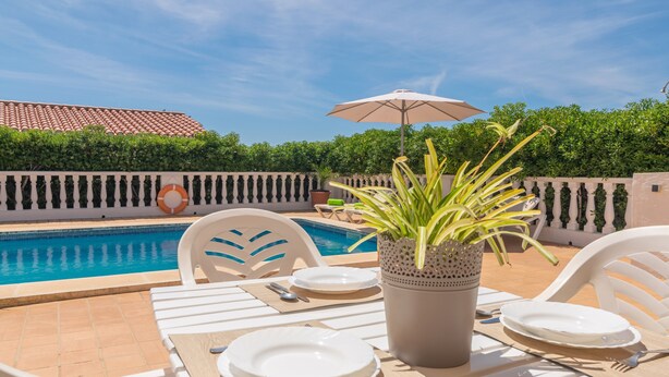 A poolside dining area with a table set for two, a potted plant, and a lifebuoy on the wall. - VILLA VICTORIA - Charming house with shared pool. (Alaior)
