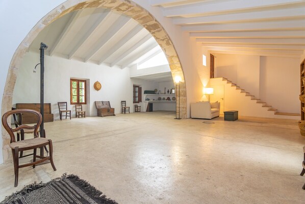 An open-plan living area with a high ceiling, exposed beams, and a staircase leading to an upper level.