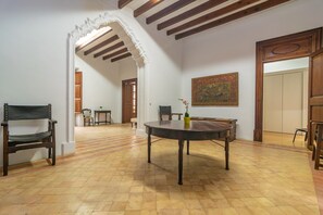 A spacious room with a wooden floor, a round table, and a chair. There is a door leading to another room and a painting on the wall.