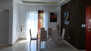 Ein modernes Wohnzimmer mit Essbereich, ausgestattet mit einer Couch, Sesseln, einem Couchtisch und einem Fernseher.