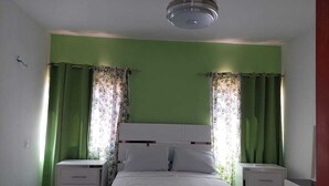 Ein Schlafzimmer mit einem Bett, zwei Nachttischen, einem Deckenventilator und grünen Vorhängen.