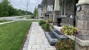 Une rue résidentielle avec un trottoir pavé, des maisons aux façades en pierre et des jardinières fleuries.