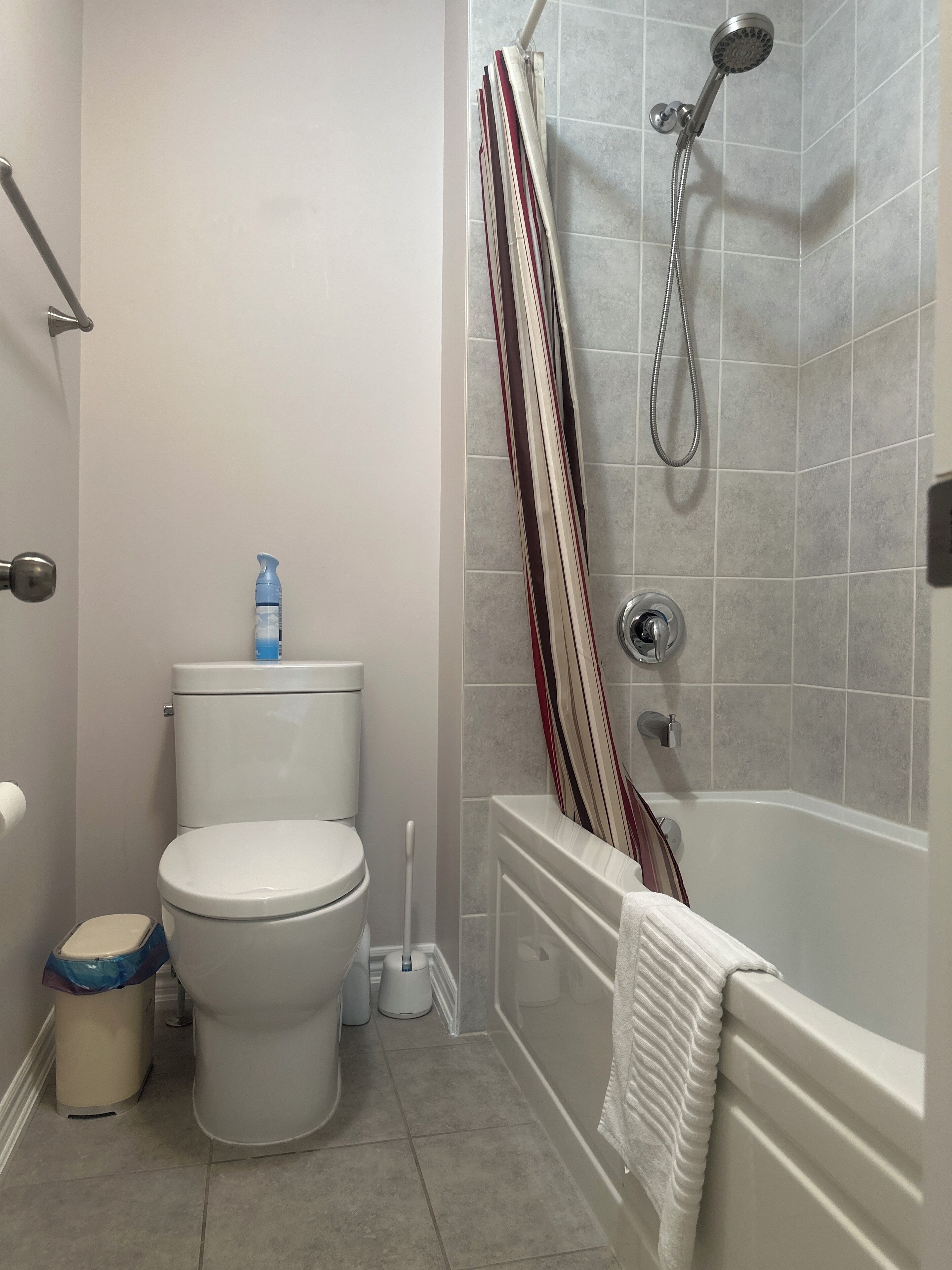 A bathroom with a toilet, a bidet, a shower with a striped curtain, and a bathtub.