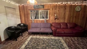 A cozy room with a purple sofa, a red leather couch, a black chair, and a patterned rug. - Cozy retreat with canyon views, sound of the river, and the smell of the pines.  (Wallace)
