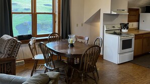 Un comedor con una mesa y sillas de madera, una cocina con estufa blanca, y un ventanal con cortinas.