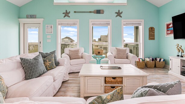A living room with a light blue wall, two white sofas, a coffee table, and a view of the outside. - Sweetheart savings! 3 min walk to Beach, Ocean View, WIFI, King 🛏 (Crystal Beach)